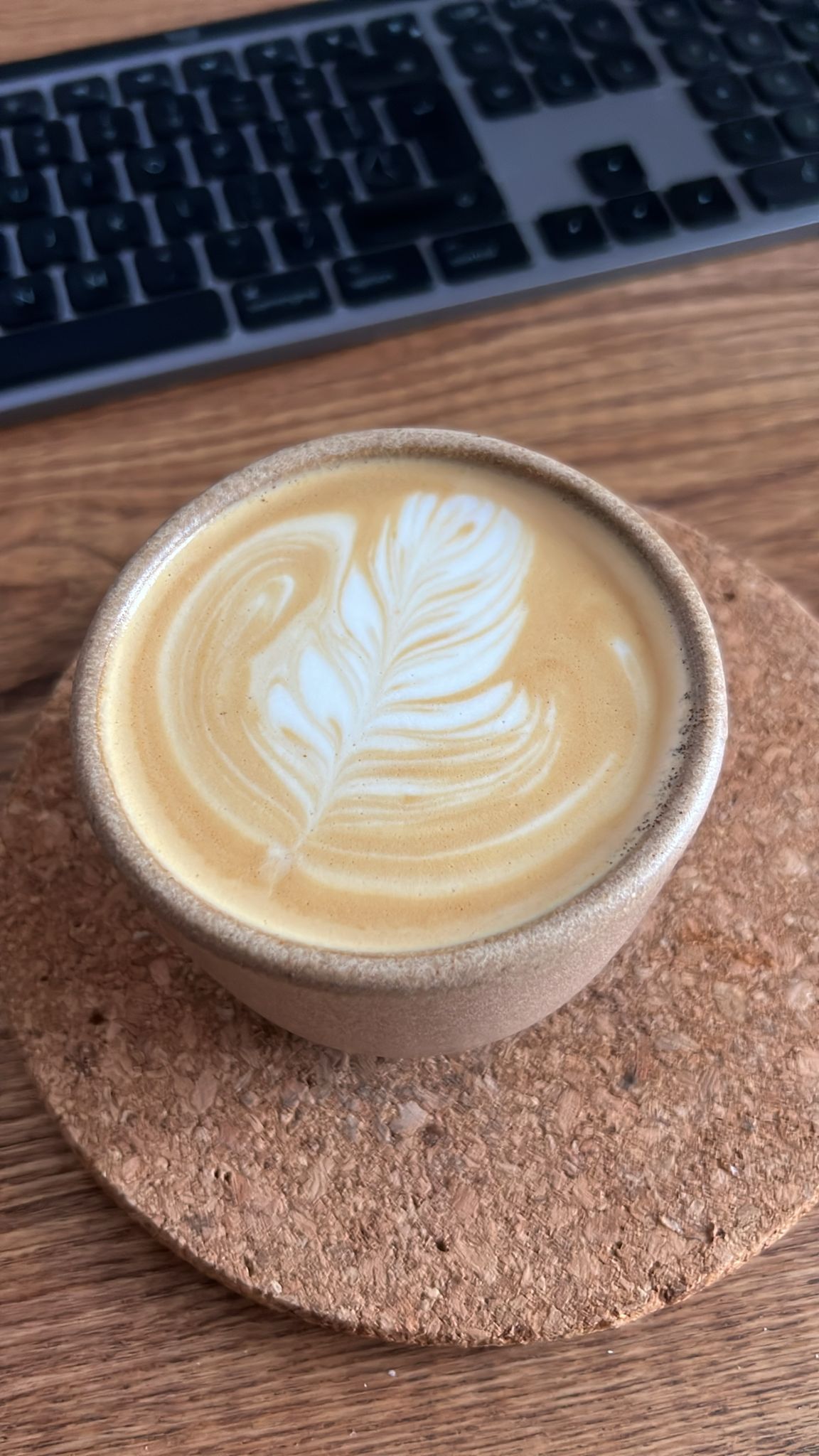 Feather latte art in a ceramic cup on a cork coaster